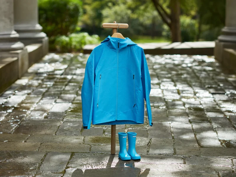 Kleine Regenjacke und Gummistiefel auf nassem Kopfsteinpflaster an der Haustür