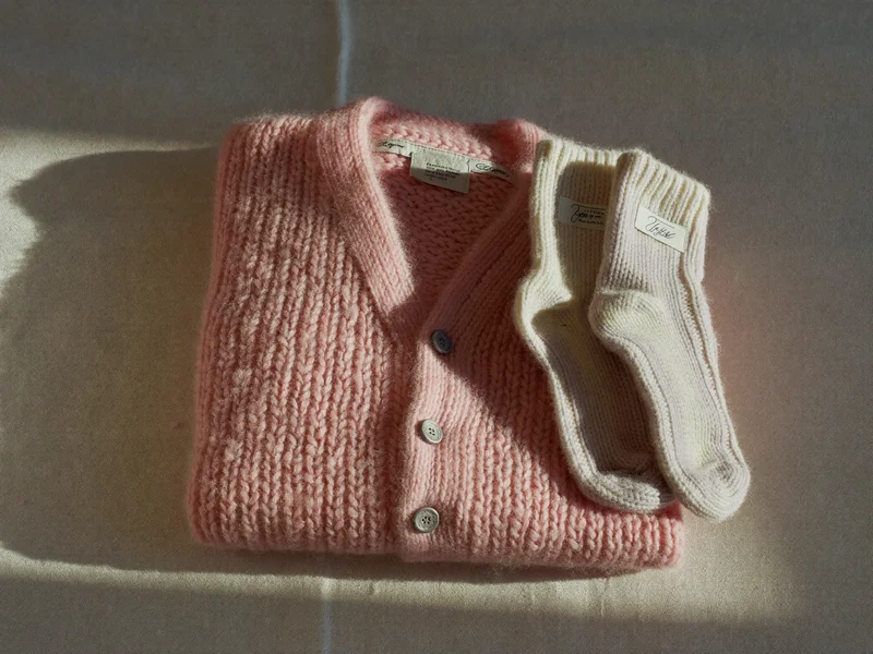 Gestricktes Pastell-Jäckchen und Wollsöckchen ordentlich gestapelt auf Leinendecke