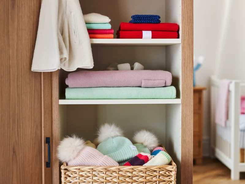 Ordentlich gefaltete Kinderkleidung und Mützenkorb im Regal einer Kindergarderobe